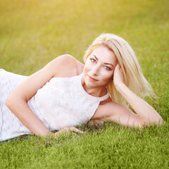 Pretty young woman lying at grass meadow. Light dress. Green background. Harmony face. Blonde hair. Summer time. Copyspace. Dream about vacation. Backyard relax concept. Female portrait 