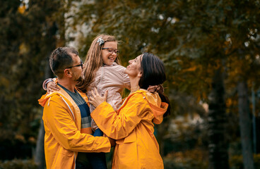 Family of three in raincoat enjoying together in city park after rain.
