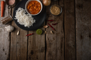 Tasty chicken curry with boiled rice on rustic wooden table with spices background. Dinner with traditional Indian dish. Exotic delicious. Food concept. View from above. Space for text. Flat lay.