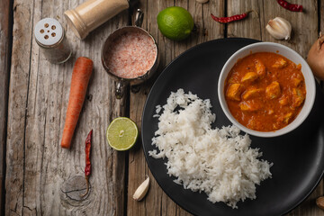 View from above of hot chicken curry with boiled rice on rustic wooden table with spices background. Dinner with traditional Indian dish. Exotic delicious. Food concept. Restaurant menu. Flat lay.
