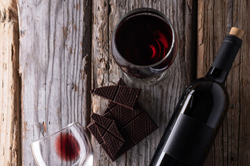 View from above of elegant bottle and wineglasses of red wine with dark chocolate on rustic wooden...