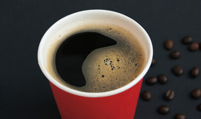 Disposable red cup with fresh hot black coffee and roasted beans on a black background. The concept of coffee to go