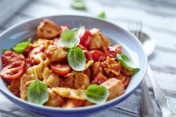 Farfalle pasta with chicken breast, cherry tomatoes and fresh basil. Bright wooden background. Close up. 