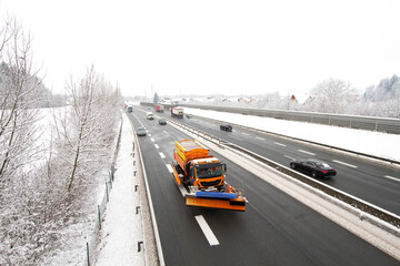 Snow plow spreading the sand on the highway in front of the vehicles. Snowplow clearing the road.
