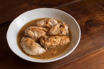 Overhead view of cooked chicken in vegetable sauce with cognac on white dish and a wooden table. Cooking recipes at home. Food presentation.