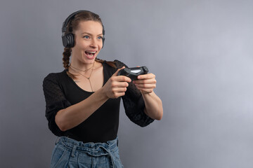Emotional smiling gamer woman playing video game and using joystick and headphones on grey background. Gambler concept. Using modern technology. © Anton
