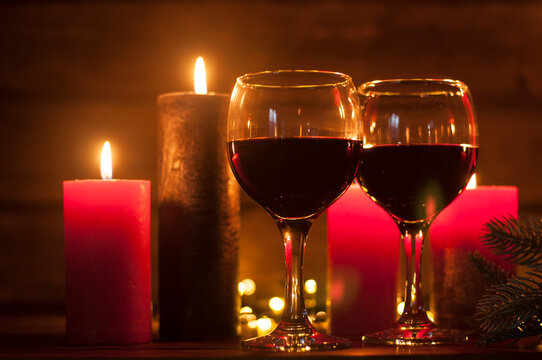 Glasses of red wine on a wooden table. Burning candles and decorations in the background. New Year or Christmas holiday. Valentine