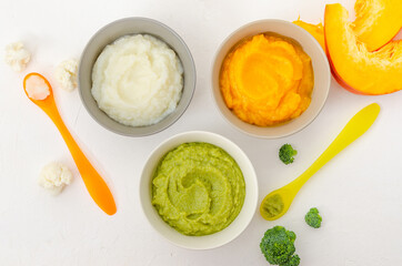 Baby food. Variation of the three homemade vegetable puree in bowls. Pumpkin puree, cauliflower puree and broccoli puree on a white background. Top view.