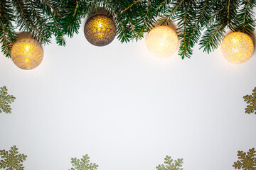 Branches of spruce with glowing baubles lying on the Christmas background. White background with shiny snowflakes.