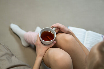 Girl's hands hold a cup of tea in a brown bed