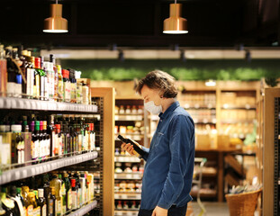 Supermarket shopping, face mask and gloves,Young man shopping in supermarket, reading product information.