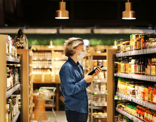 Supermarket shopping, face mask and gloves,Young man shopping in supermarket, reading product information.