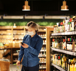Supermarket shopping, face mask and gloves,Young man shopping in supermarket, reading product information.