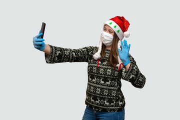 woman in a Christmas hat communicates via video link or chatting with smartphone. young girl on isolation takes a selfie. Coronavirus and Christmas concept.