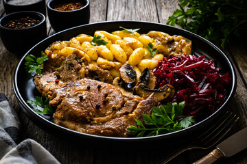 Roasted pork steaks, noodles and pickled beetroot and onion on wooden table
