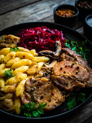 Roasted pork steaks, noodles and pickled beetroot and onion on wooden table
