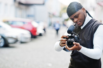 Young professional african american videographer holding professional camera with pro equipment. Afro cameraman wearing black duraq making a videos.