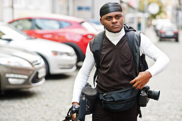 Young professional african american videographer holding professional camera with tripod pro equipment. Afro cameraman wearing black duraq making a videos.