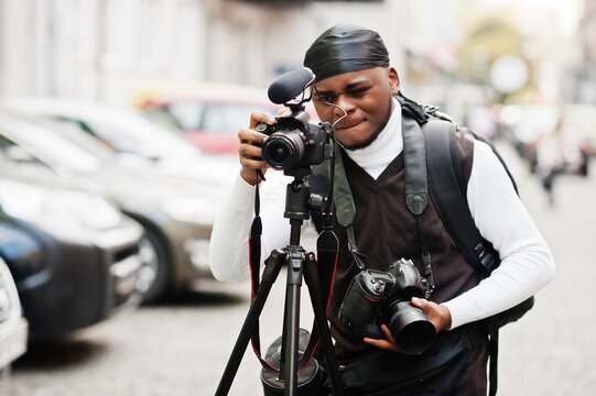 Young professional african american videographer holding professional camera with tripod pro equipment. Afro cameraman wearing black duraq making a videos.