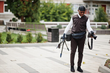 Young professional african american videographer holding professional camera with pro equipment. Afro cameraman wearing black duraq making a videos.