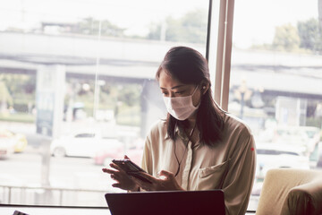 Asian woman with face mask working with notebook laptop in cafe. Concept for new normal and life in...