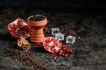 Hookah ceramic head fulled with aromated molose, pomegranade, blueberry and ice cubes on the grunge black table with smoke.