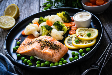 Steamed salmon steak with cauliflower, broccoli, carrots, lemon, peas and mayonnaise on wooden table 
