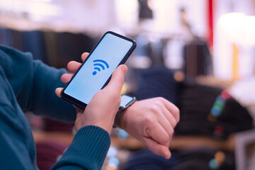 Man holds a smartphone with a close-up wi-fi icon and a smart watch on his hand.