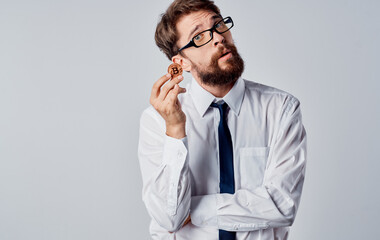 A man with a gold coin in his hands on a light background puzzled look of the Bitcoin cryptocurrency business