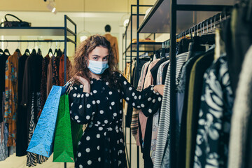 Young beautiful woman in a protective mask on her face, chooses clothes in the store, makes safe purchases