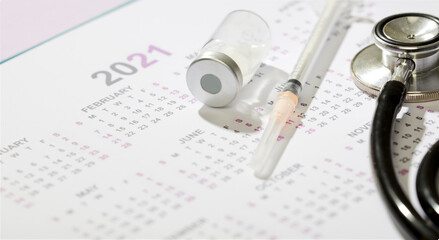 Syringe and vaccine in glass vial, with stethoscope on calendar year 2021, (vaccine campaign), blue background
