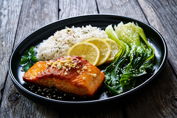 Fried salmon steak with lemon, basmati rice and steamed pak choi cabbage served on wooden table
