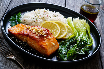 Fried salmon steak with lemon, basmati rice and steamed pak choi cabbage served on wooden table
