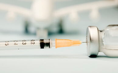Vaccine in glass vial, with syringe, white plane, blue background.