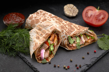 Shawarma with meat, cutaway, with sauce, tomatoes, cheese, herbs and garlic, on black slate, on a...