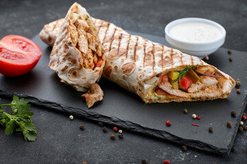 Shawarma with meat, cutaway, with sauce, tomatoes, cheese, herbs and garlic, on black slate, on a...