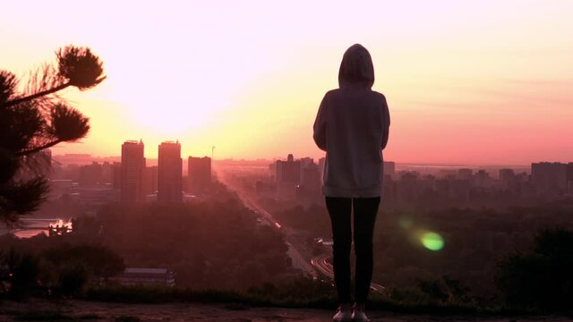 silhouette woman in casual hoodie standing on hill enjoy view on urban city at sunrise