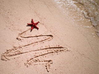 Christmas tree drawn in sand at the beach. Holiday concept.