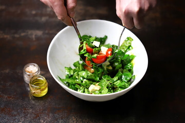 Salad in a white bowl mixed by the hands of the cook. Cooking a healthy salad. Fitness food. Healthly food.