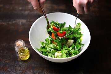 Salad in a white bowl mixed by the hands of the cook. Cooking a healthy salad. Fitness food. Healthly food.