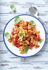 Farfalle pasta with chicken breast, cherry tomatoes and fresh basil. Bright wooden background. Top view.