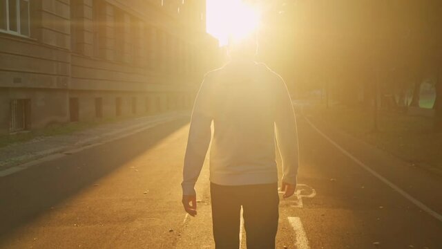 back view man with french bulldog walking on the street in empty morning city walks at sun rays slow motion