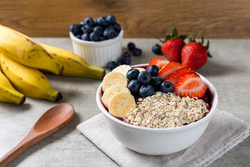 Brazilian frozen açai berry ice cream bowl with strawberries, bananas, blueberry and oatmeal flakes. with fruits on wooden background. Summer menu front view