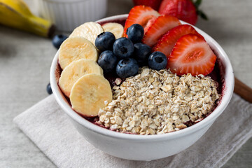 Close up Brazilian frozen açai berry ice cream bowl with strawberries, bananas, blueberry and oatmeal flakes. with fruits on wooden background. Summer menu front view