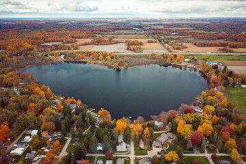 Beautiful full aerial view of the heart shaped Saugany Lake in Indiana surrounded by residential homes and autumn colored trees or foliage with fluffy white clouds in the sky above.
