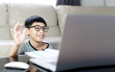 asian boy is using a laptop and communicates on the Internet at home.smile boy is using a laptop and study online with video call teacher at home. homeschooling, distant learning