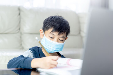 asian boy doing homework with computerlaptop at home. Child using gadgets to study.Education and distance learning for kids. Homeschooling during quarantine. Stay at home entertainment.child with mask