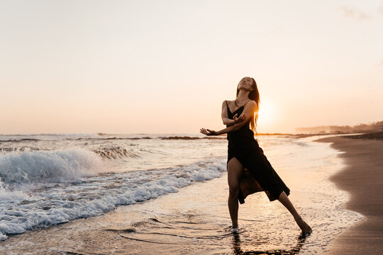 Freedom Chinese Woman Feeling Free Dancing In Black Elegant Dress At Beach Sunset. Healthy Living Asian Girl On Summer Travel Vacation. Success, Happiness, Mindfulness Concept.