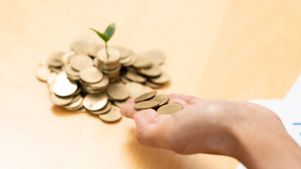 Hands of businessman putting coin into plant sprouting growing up to profit, demonstrating financial growth through saving plans and investment schemes.
