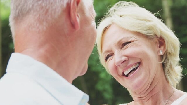 Close up of loving senior couple hugging and kissing in garden at home together - shot in slow motion